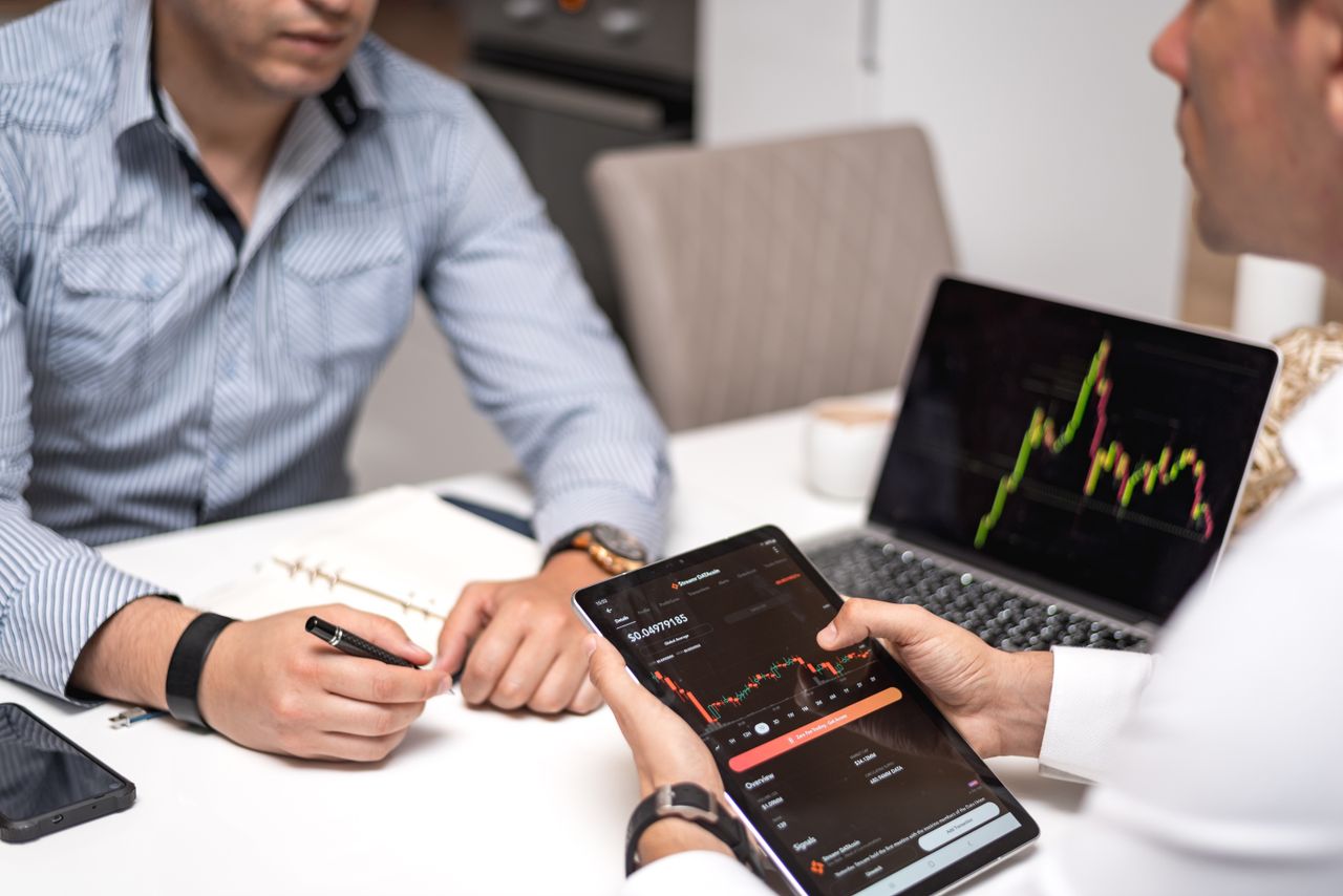 About Two professionals discussing crypto trends using digital devices in an office setting.