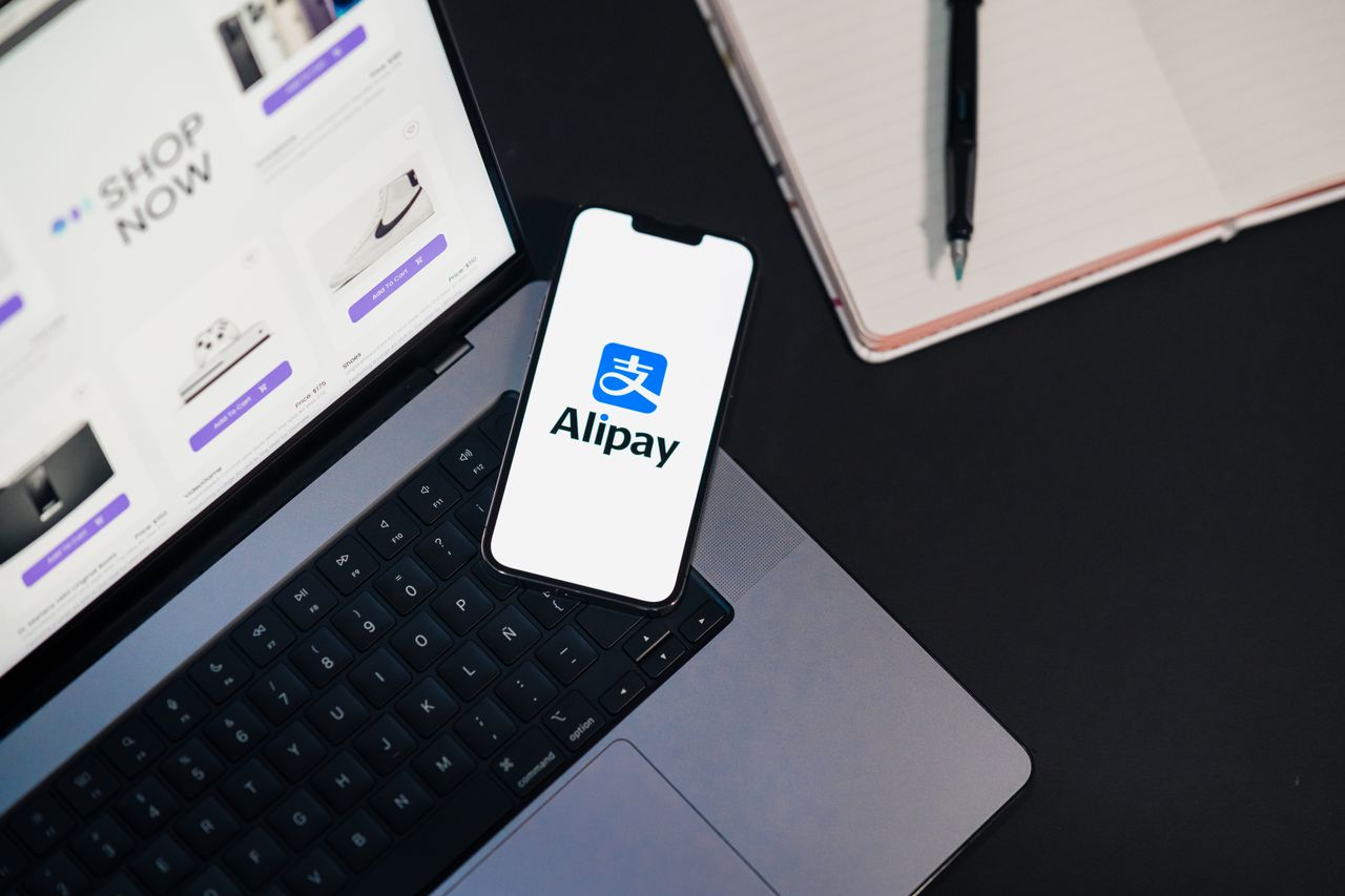 What Is Fintech? A Beginner’s Guide to Financial Technology Smartphone displaying Alipay app on open laptop with online shopping site.