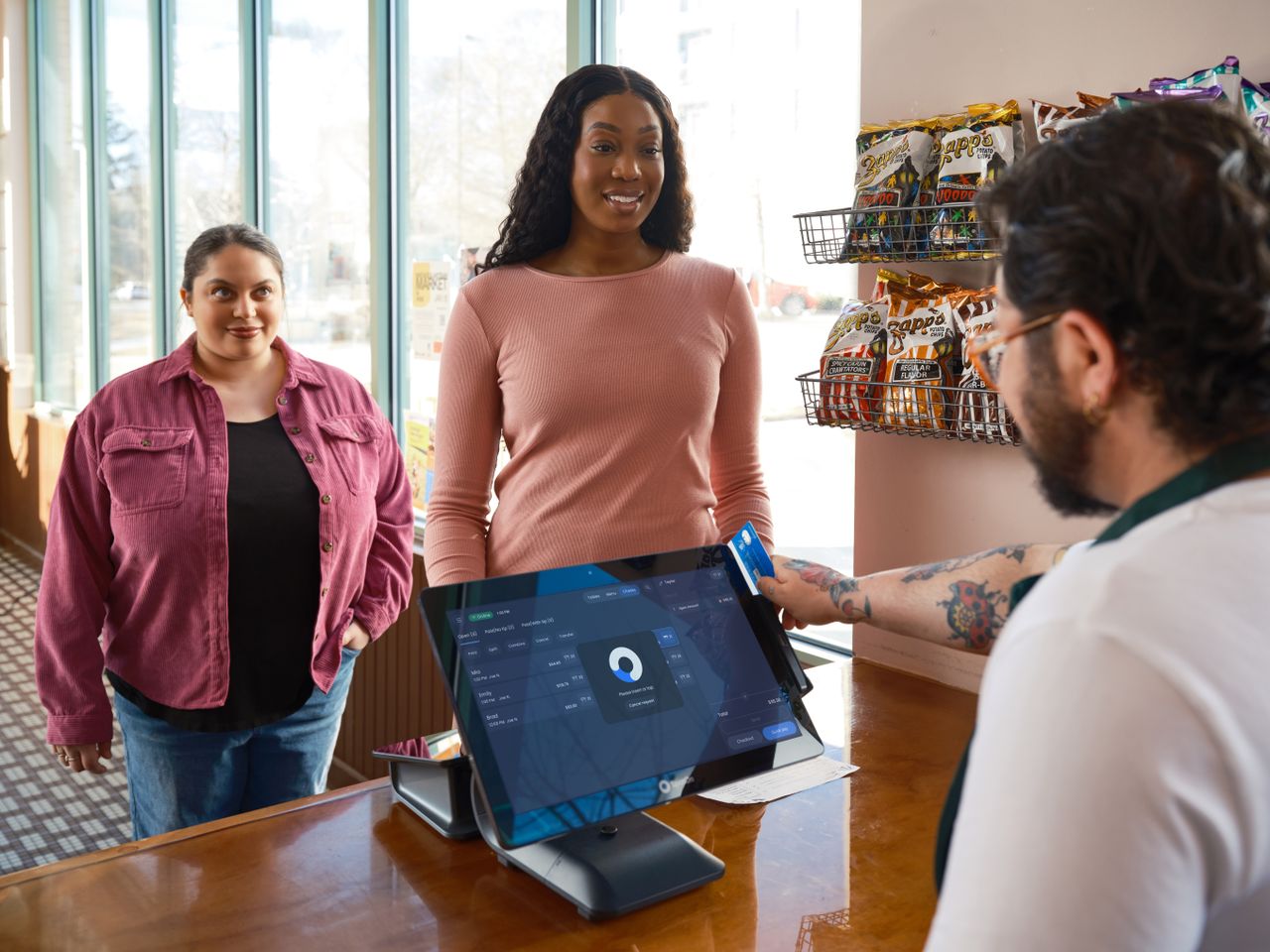 Two women making a payment at a convenience store using a touch screen POS system.